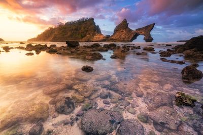 Rocks on beach against sky during sunset