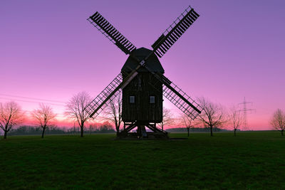 Traditional windmill on field against sky during sunset