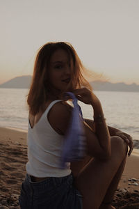 Woman wearing sunglasses at beach against sky during sunset