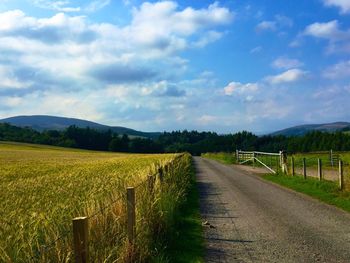 Empty road amidst field against sky