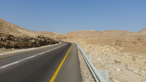 Empty road amidst mountains against clear sky on sunny day