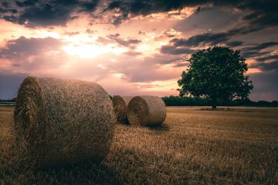 Hay bales on field against sky at sunset