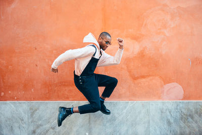 Side view of young man jumping against wall