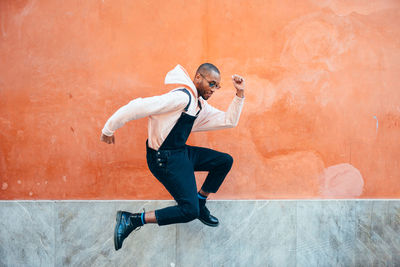 Full length of young man jumping against wall