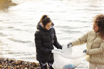 Smiling female environmentalists collecting microplastics against lake