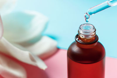 Bottle with serum and pipette on a blue and pink background close-up.