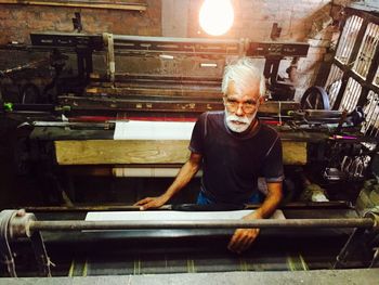 High angle view of senior man working with loom at illuminated workshop