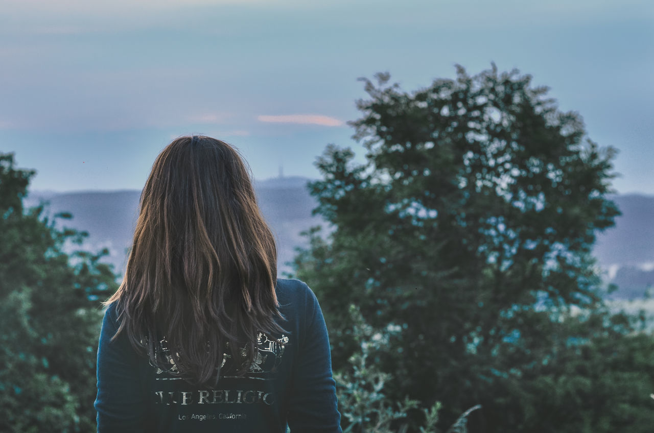 tree, plant, one person, real people, lifestyles, rear view, sky, leisure activity, long hair, hairstyle, hair, standing, nature, women, adult, focus on foreground, waist up, casual clothing, outdoors, looking at view, teenager