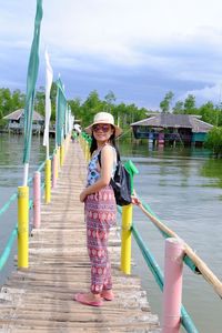 Full length portrait of young woman standing over lake on footbridge