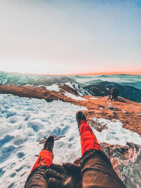 Low section of person on snowcapped mountain against sky