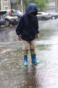 Boy wearing raincoat standing on city street during rainy season