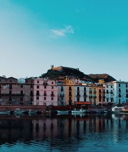 Buildings by river against blue sky