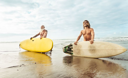 Men holding surfboards on beach against sky