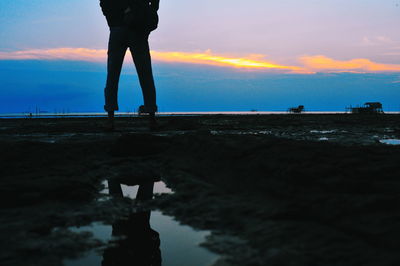 Low section of silhouette man standing by sea against sky