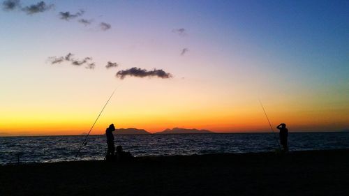 Silhouette men fishing on beach against sky during sunset