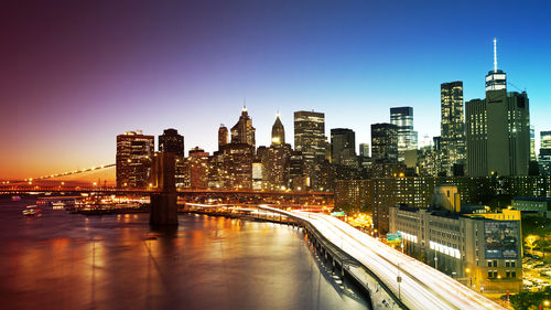 Illuminated bridge and buildings against sky in city