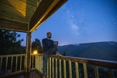 Man standing by railing against sky at night