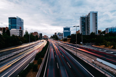 Light trails on road amidst buildings in city against sky