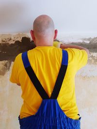 Rear view of person standing against yellow wall