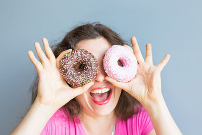Cheerful woman holding donuts against wall