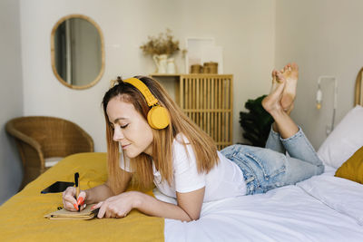 Young woman using mobile phone while sitting on bed at home