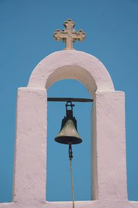 Low angle view of bell and white wall against blue sky