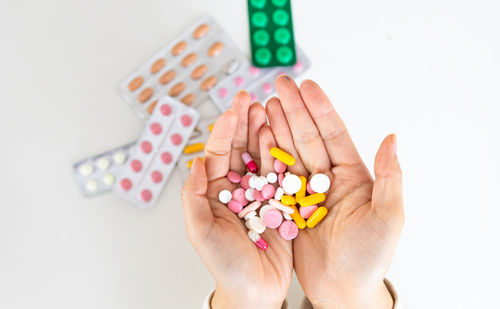 Cropped hands of woman holding pills against white background