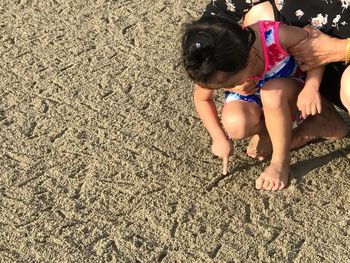 Daughter playing with sand by mother at beach