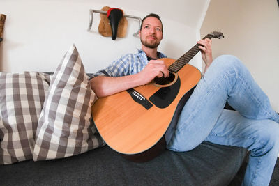 Man playing guitar on sofa at home