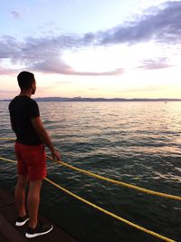 Rear view of man standing on sea against sky during sunset