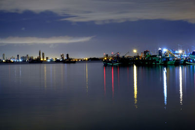 Illuminated buildings by sea against sky at night