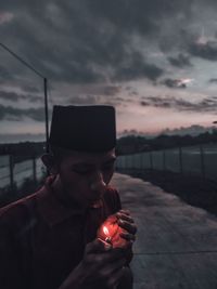 Young man igniting cigarette lighter at dusk