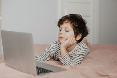 Little boy lie in the bedroom on the bed and look at the laptop. high quality photo