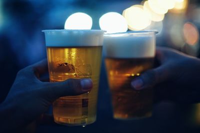 Cropped hands toasting beer glasses at night