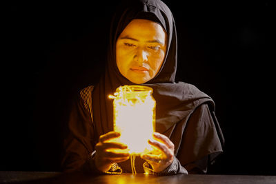 Muslim woman looking at a jar of light in the dark
