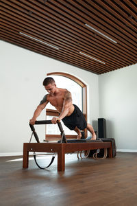 Full length of shirtless man sitting on wooden floor