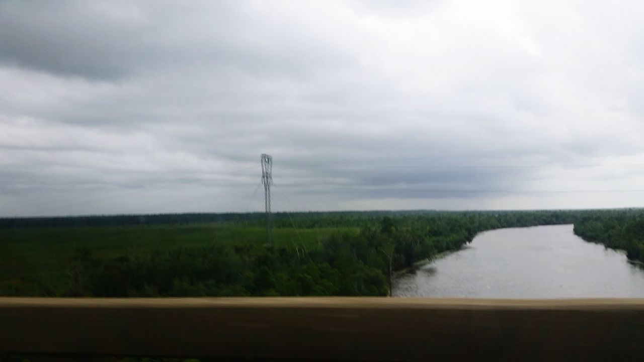 sky, cloud - sky, tranquil scene, tranquility, grass, water, cloudy, landscape, field, scenics, cloud, nature, beauty in nature, plant, overcast, day, lake, weather, non-urban scene, idyllic