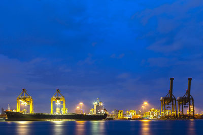 Illuminated city by sea against sky at night