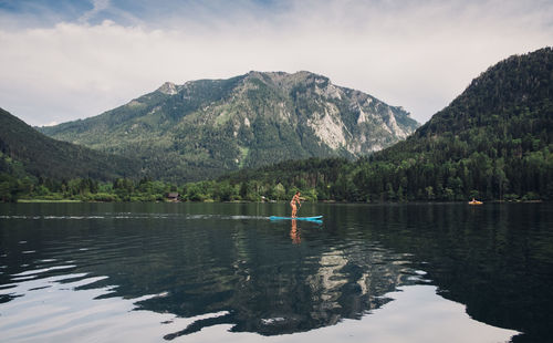 Woman paddleboarding in lake by mountains against sky