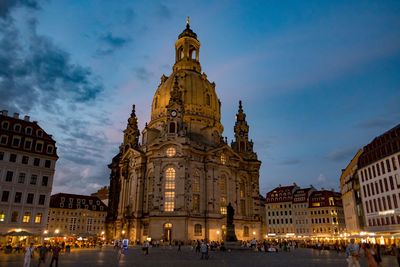 People walking by cathedral and buildings against sky in city