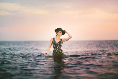 Young woman in sea against sky during sunset