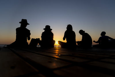 Silhouette people sitting against clear sky during sunset