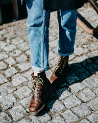 Low section of woman wearing shoes while standing on cobbled footpath