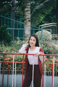 Portrait of smiling young woman standing against railing