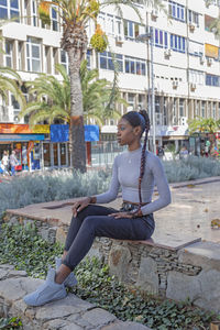 Full length of woman sitting against building in city