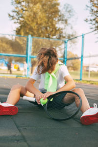 Boy with tennis racket sitting in court