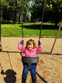 Portrait of happy girl playing on swing in park