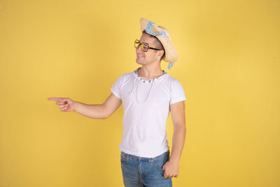 Young woman wearing sunglasses standing against yellow wall