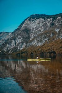 People on lake by mountains against sky