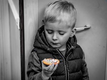Cute boy holding cookie while standing against door at home